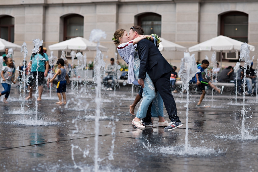 A couple kiss in the fountain at Dilworth Park as children play in the background.